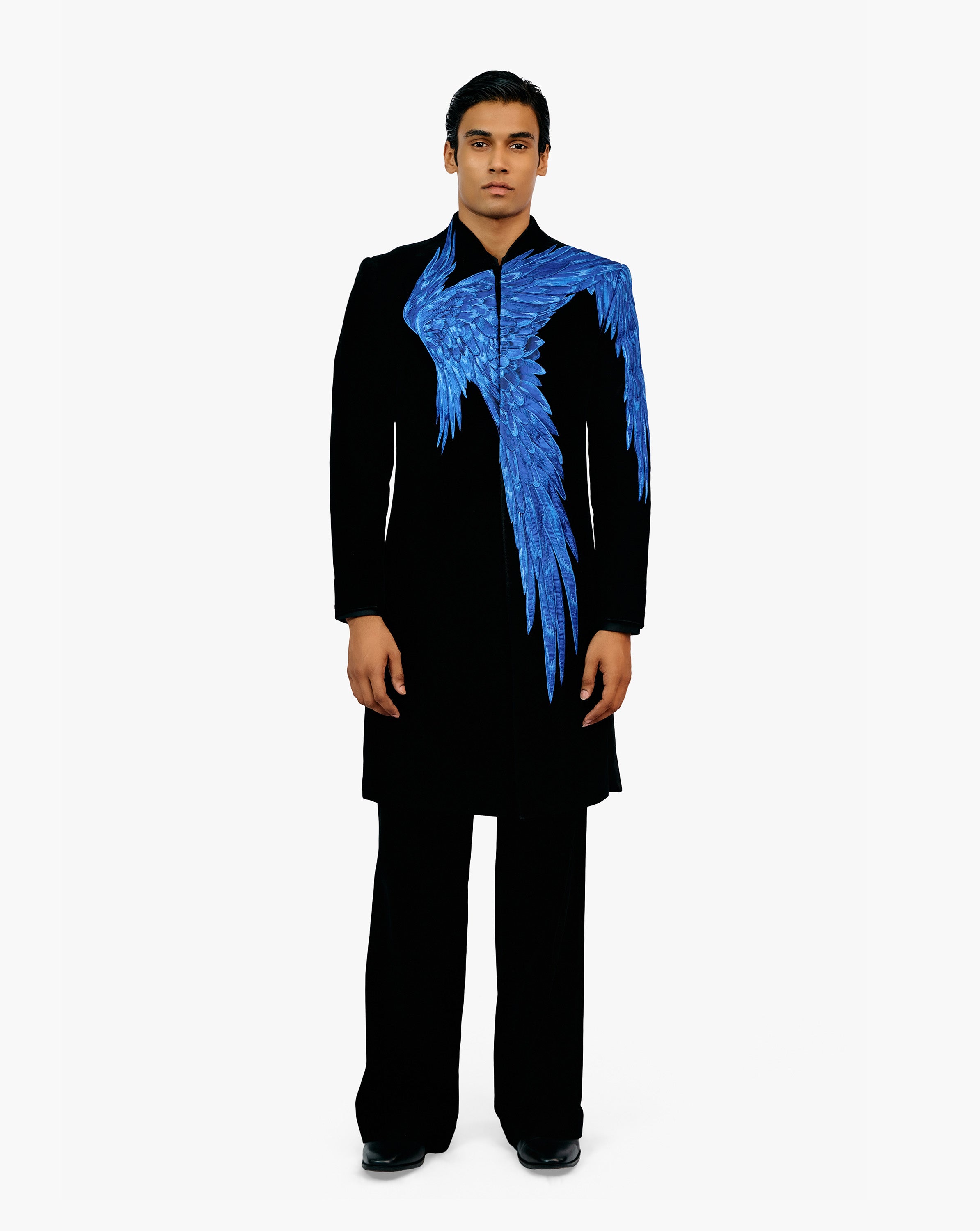 Model wearing a black suit with blue feather-like detailing on the coat